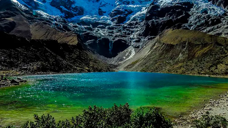 Paisaje de la laguna Humantay con aguas turquesas y montañas nevadas en el fondo.