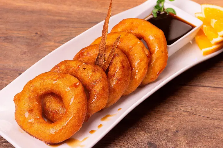 Picarones en forma de aros cubiertos con miel de chancaca.