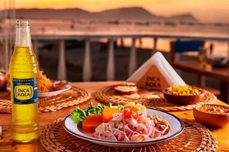 Botella personal de vidrio de Inca Kola, la bebida gaseosa tradicional de Perú, acompañando un plato de comida peruana.