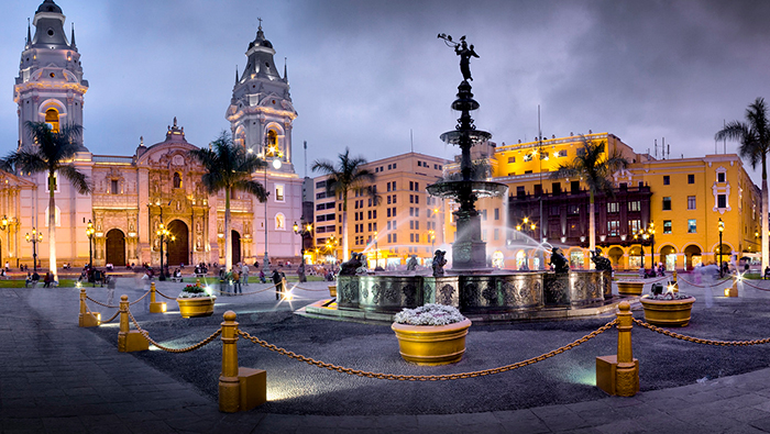 Vista nocturna de la Plaza de Armas de Lima con la fuente iluminada en primer plano y la catedral al fondo.