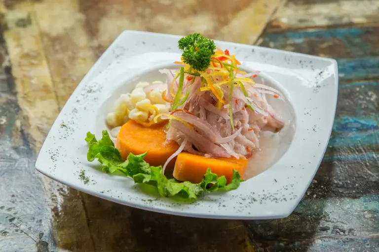 Plato de ceviche peruano con pescado fresco, cebolla morada, choclo y camote.
