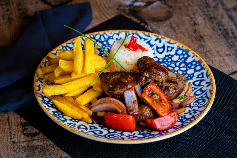 Porción de lomo saltado con papas fritas, cebolla y tomate en un plato típico peruano.